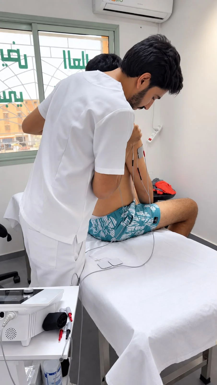 Abdellatif Edlaoui accompagnant un patient assis sur une table de soins chez PhysioFlex